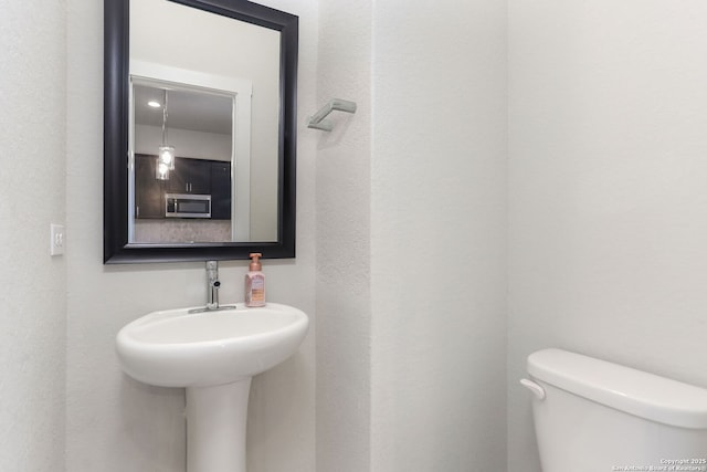 bathroom with toilet, a textured wall, and a sink