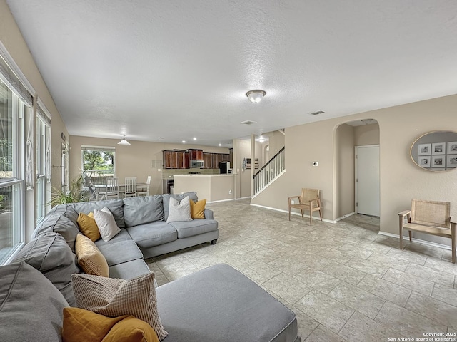 living area with arched walkways, stairs, stone tile floors, baseboards, and visible vents