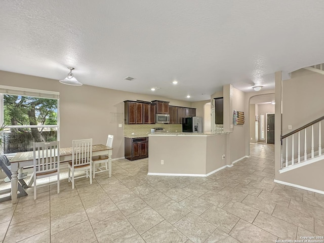 kitchen featuring stainless steel microwave, tasteful backsplash, visible vents, dark brown cabinets, and fridge with ice dispenser