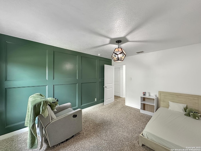 bedroom featuring visible vents, a decorative wall, baseboards, a textured ceiling, and light colored carpet