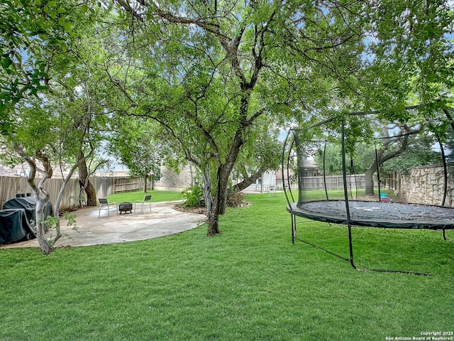 view of yard featuring a fire pit, a fenced backyard, a patio, and a trampoline