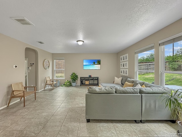 living room with a textured ceiling, visible vents, plenty of natural light, and arched walkways