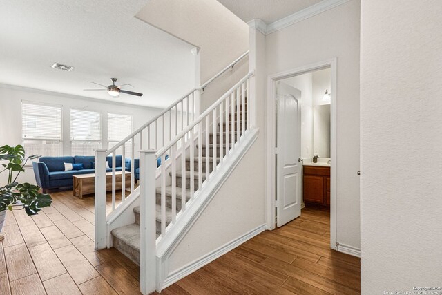 stairs with visible vents, baseboards, ornamental molding, wood finished floors, and a ceiling fan
