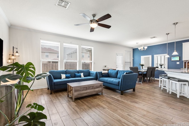 living area with visible vents, ornamental molding, ceiling fan with notable chandelier, and light wood-style floors