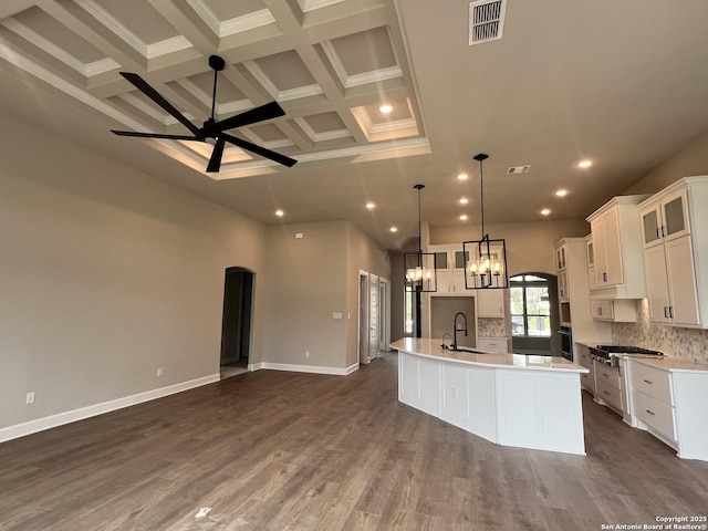 kitchen with a kitchen island with sink, beamed ceiling, black oven, ceiling fan with notable chandelier, and open floor plan