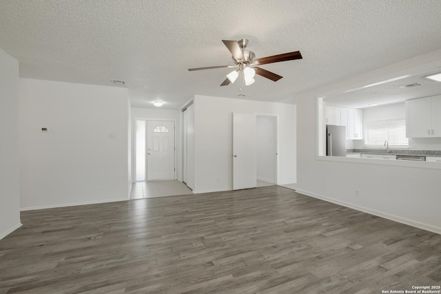 unfurnished living room featuring a textured ceiling, a sink, ceiling fan, visible vents, and wood finished floors