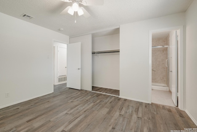 unfurnished bedroom featuring a closet, visible vents, a textured ceiling, wood finished floors, and ensuite bathroom