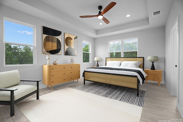 bedroom featuring visible vents, light wood-style floors, a raised ceiling, and baseboards