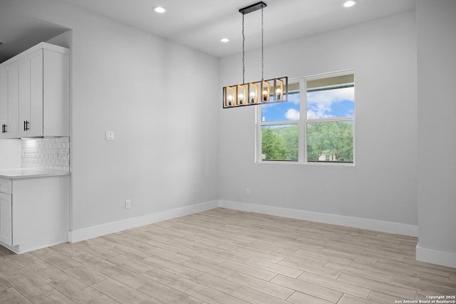 unfurnished dining area with light wood-style floors, recessed lighting, a chandelier, and baseboards
