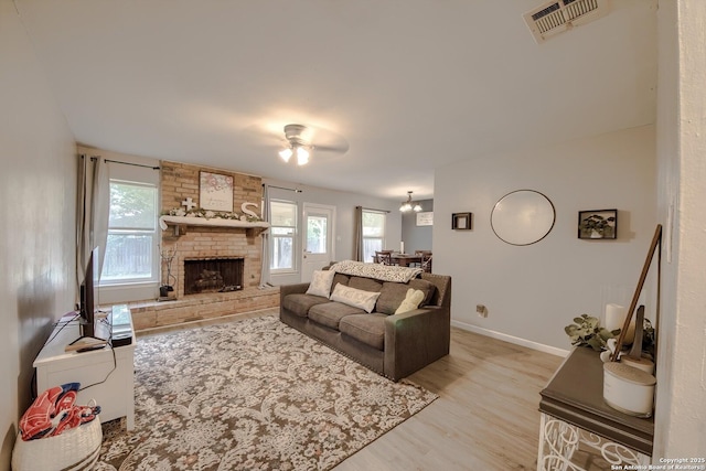 living area with a large fireplace, ceiling fan, light wood-type flooring, visible vents, and baseboards