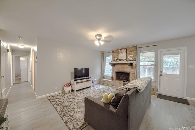 living room featuring a large fireplace, a healthy amount of sunlight, light wood finished floors, and baseboards