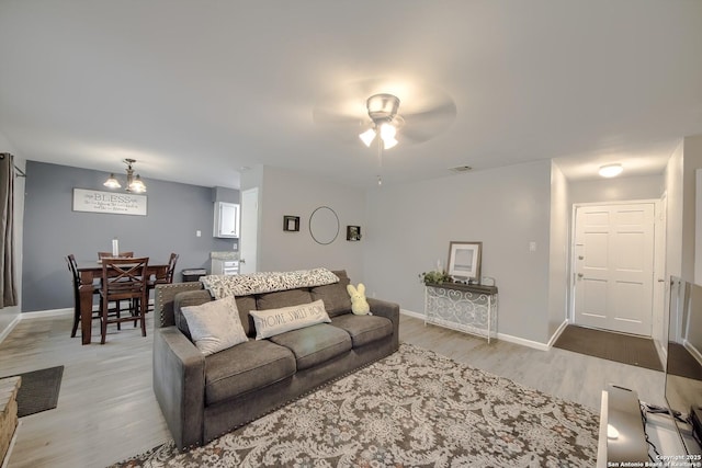 living area featuring light wood-style floors, a ceiling fan, visible vents, and baseboards