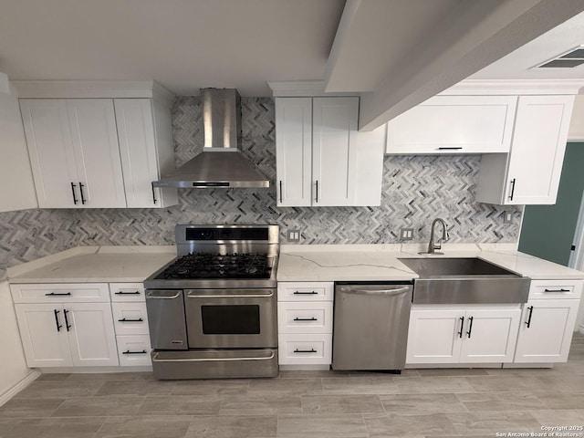 kitchen featuring wall chimney range hood, white cabinets, a sink, appliances with stainless steel finishes, and light stone countertops
