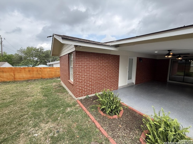 view of side of home featuring a carport, a patio area, a lawn, fence, and brick siding