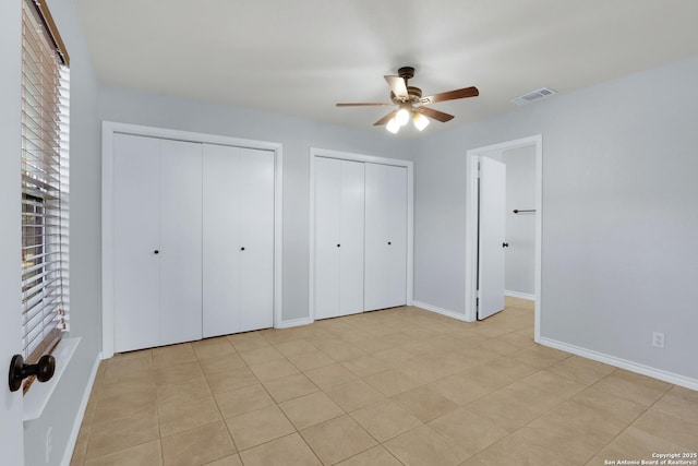 unfurnished bedroom featuring two closets, a ceiling fan, visible vents, and baseboards