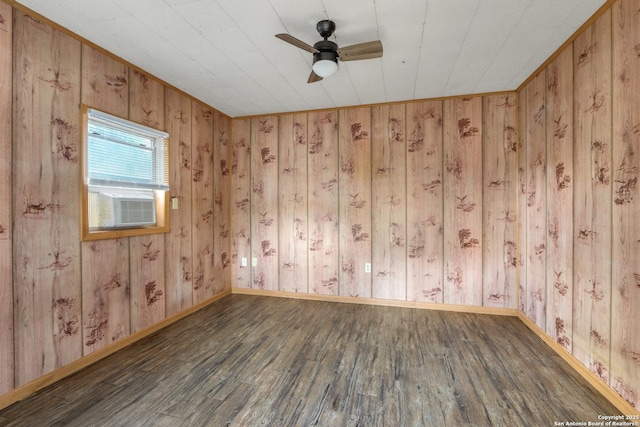 empty room featuring wooden walls, cooling unit, a ceiling fan, baseboards, and wood finished floors