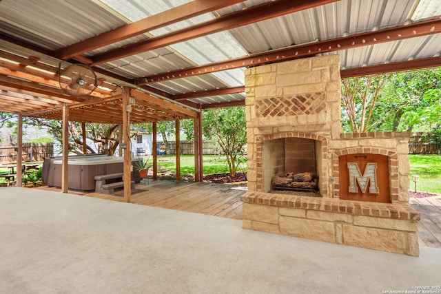 view of patio featuring an outdoor stone fireplace, fence, and a hot tub
