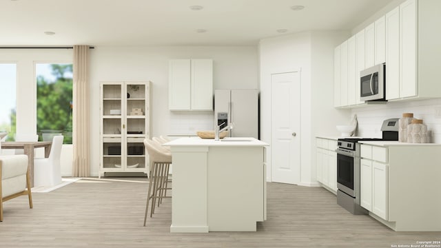 kitchen with an island with sink, backsplash, appliances with stainless steel finishes, and light wood finished floors