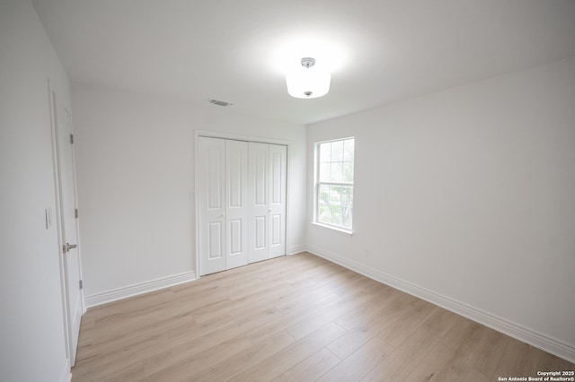 unfurnished bedroom featuring a closet, visible vents, light wood-style flooring, and baseboards