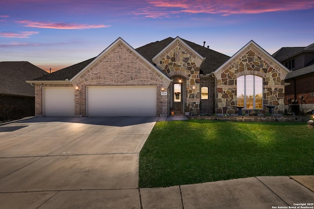 french country home with a yard, brick siding, a garage, stone siding, and concrete driveway