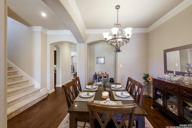 dining space featuring arched walkways, wood finished floors, a chandelier, baseboards, and crown molding