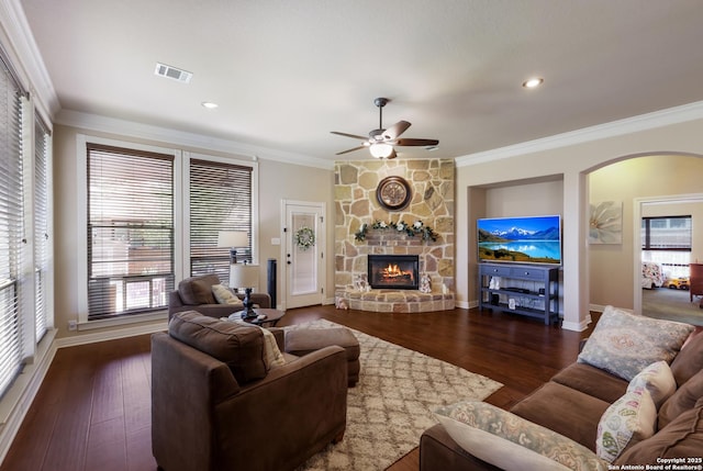 living room with ceiling fan, visible vents, a stone fireplace, baseboards, and ornamental molding