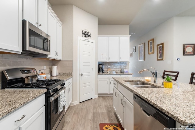 kitchen with tasteful backsplash, stainless steel appliances, light wood-style floors, a sink, and white cabinetry