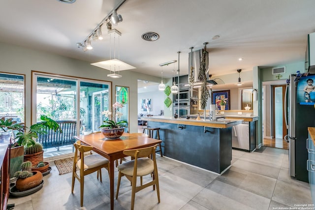 kitchen with decorative light fixtures, appliances with stainless steel finishes, light countertops, visible vents, and a kitchen breakfast bar