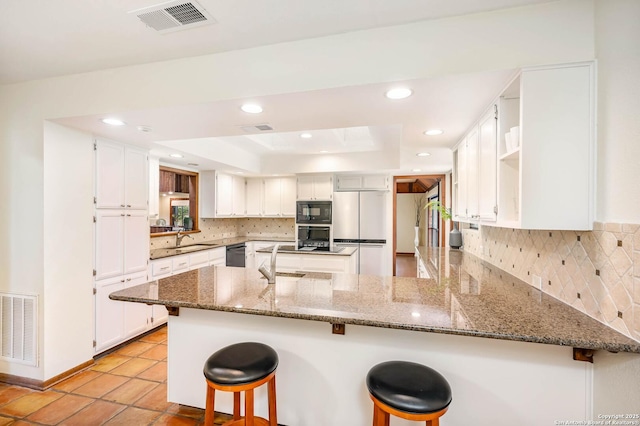 kitchen featuring fridge, black microwave, visible vents, and a peninsula