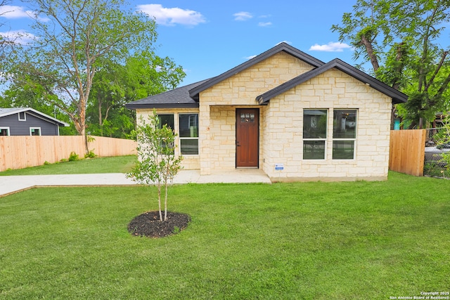 single story home with a front yard, a shingled roof, fence private yard, and stone siding
