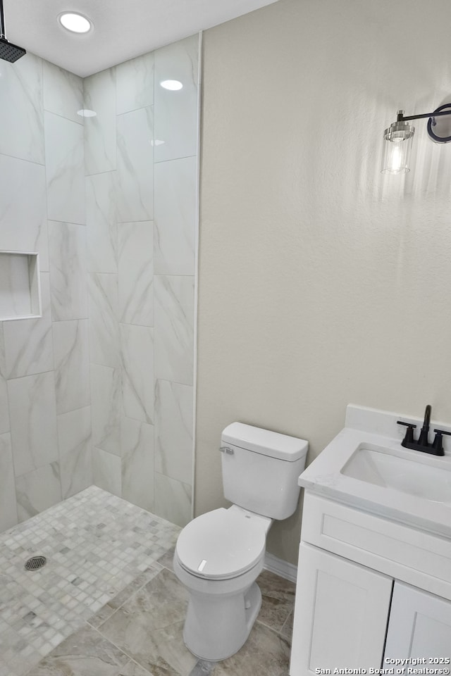 bathroom featuring toilet, a tile shower, recessed lighting, and vanity