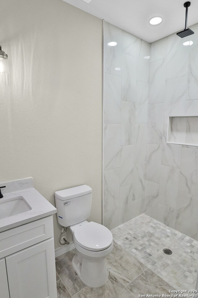bathroom with baseboards, tiled shower, toilet, and vanity