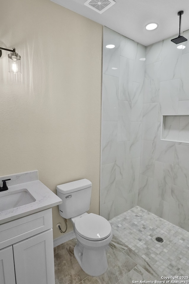 bathroom with visible vents, baseboards, toilet, vanity, and tiled shower