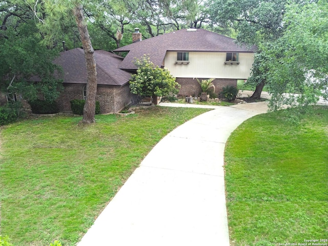 view of front facade featuring driveway, a chimney, a shingled roof, brick siding, and a front lawn