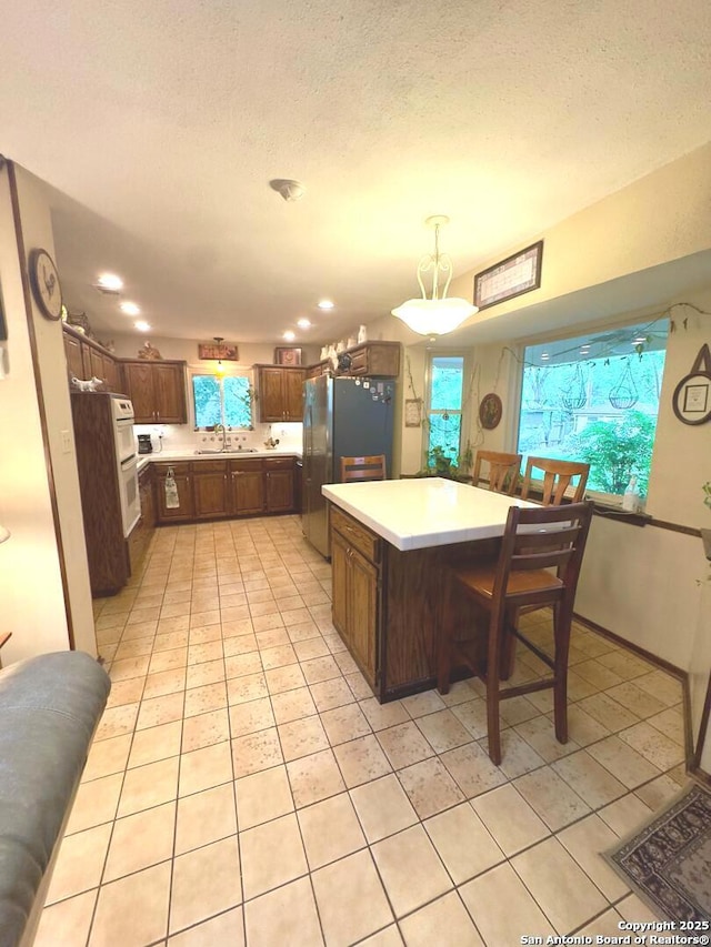 kitchen with light tile patterned flooring, light countertops, freestanding refrigerator, and a sink