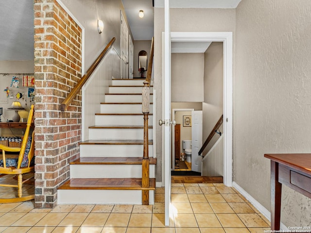 stairway featuring tile patterned flooring, a textured wall, and baseboards
