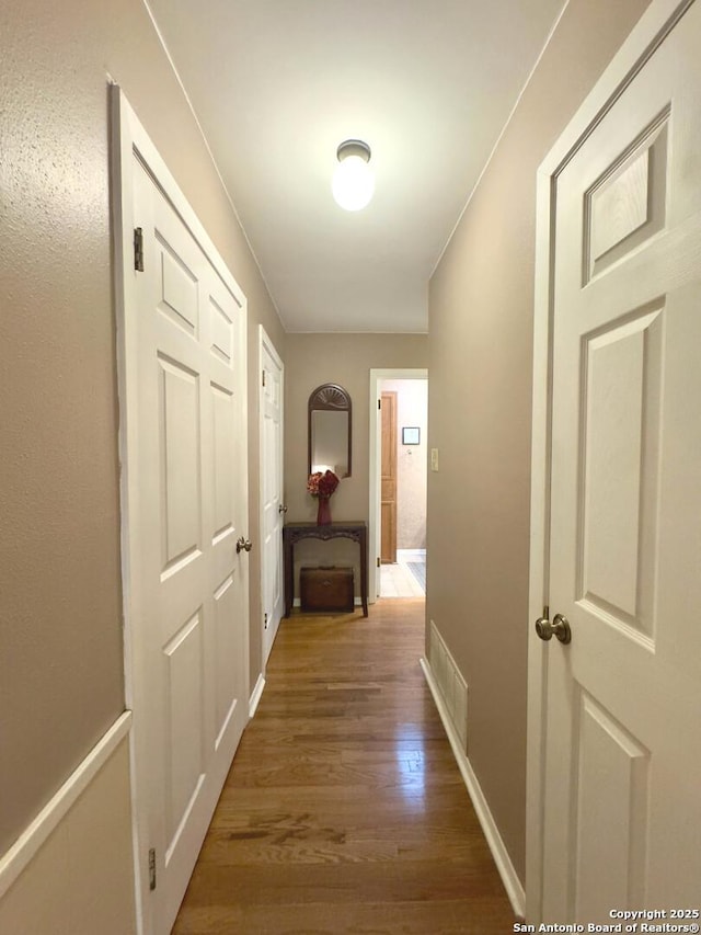 corridor featuring baseboards, visible vents, and wood finished floors