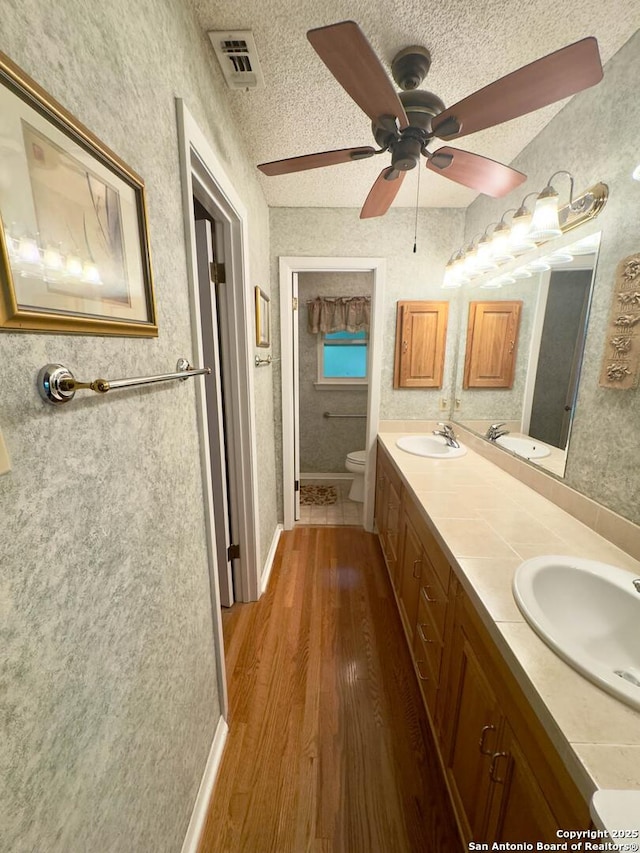 full bath with a sink, double vanity, visible vents, toilet, and wood finished floors
