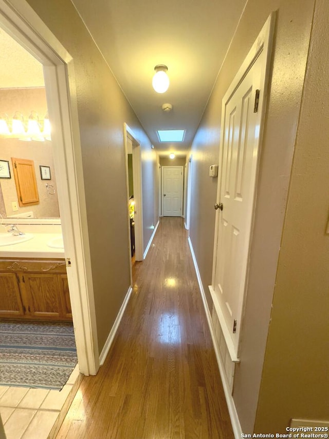 corridor with baseboards, wood finished floors, and a sink