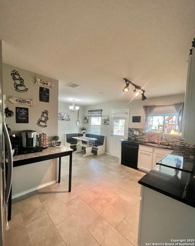 kitchen with black dishwasher, white cabinets, dark countertops, a sink, and a notable chandelier