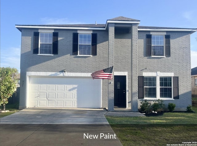 traditional-style home with a garage, brick siding, a front yard, and concrete driveway