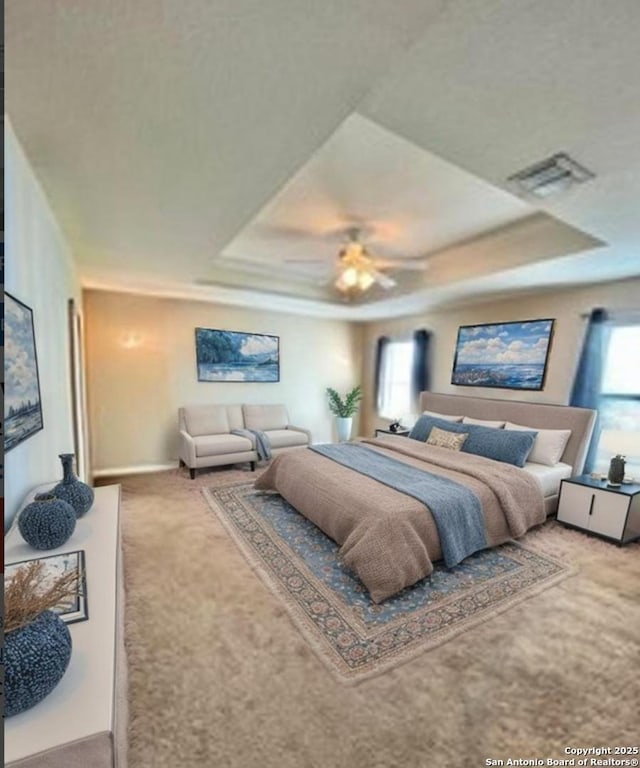 bedroom with a raised ceiling, visible vents, baseboards, carpet, and a ceiling fan