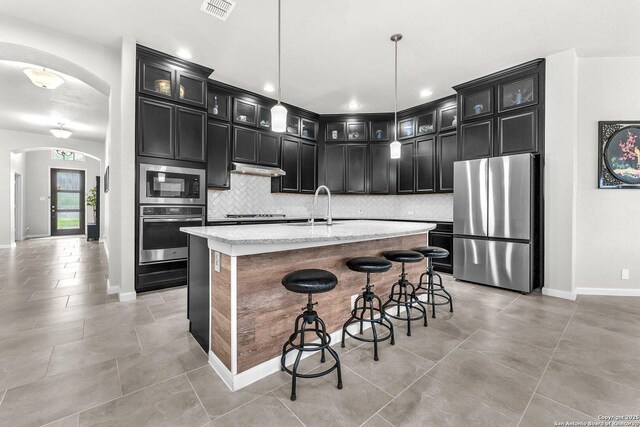 kitchen with dark cabinetry, arched walkways, appliances with stainless steel finishes, and a sink