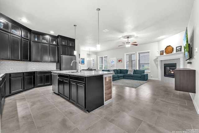 kitchen with dark cabinetry, backsplash, open floor plan, a ceiling fan, and stainless steel dishwasher