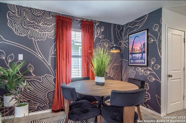dining area featuring an accent wall, wood finished floors, wallpapered walls, and baseboards