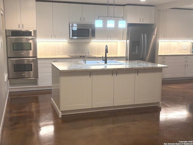 kitchen with light stone countertops, appliances with stainless steel finishes, backsplash, a sink, and a center island with sink