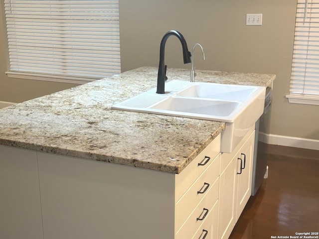 kitchen featuring dark wood finished floors, light stone countertops, white cabinets, a sink, and baseboards