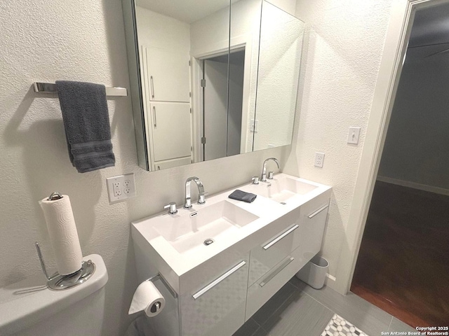 full bath with double vanity, a sink, and a textured wall