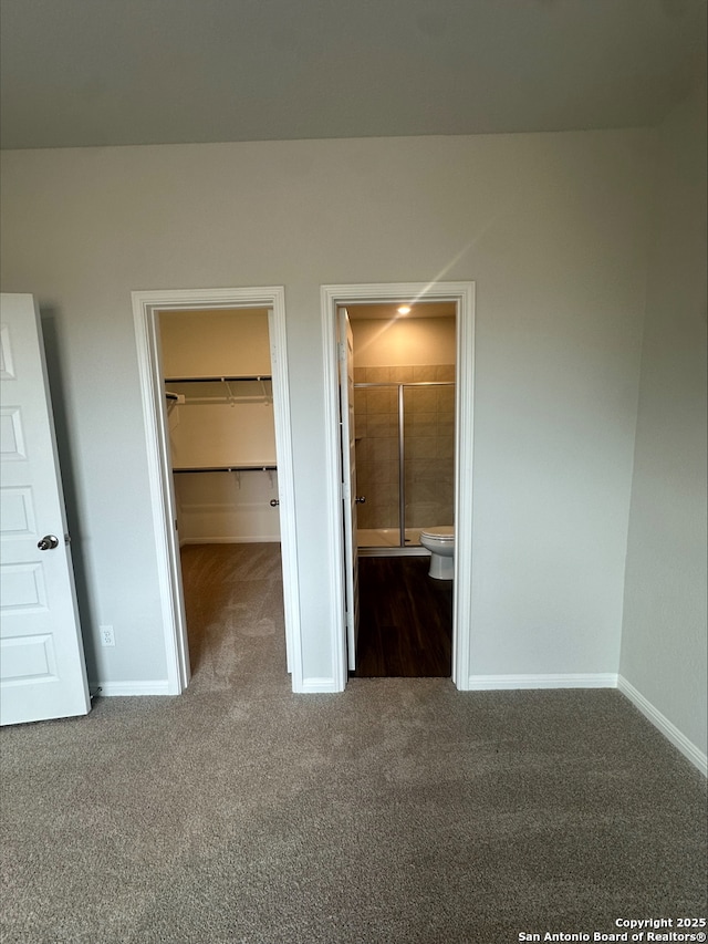 unfurnished bedroom with baseboards, carpet floors, a closet, ensuite bathroom, and a walk in closet