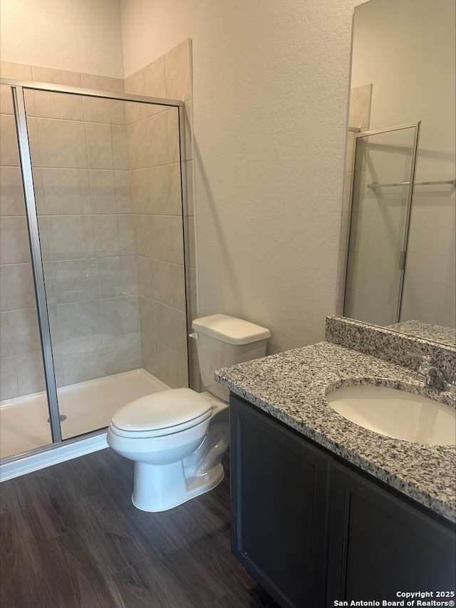 bathroom with a textured wall, a stall shower, toilet, wood finished floors, and vanity